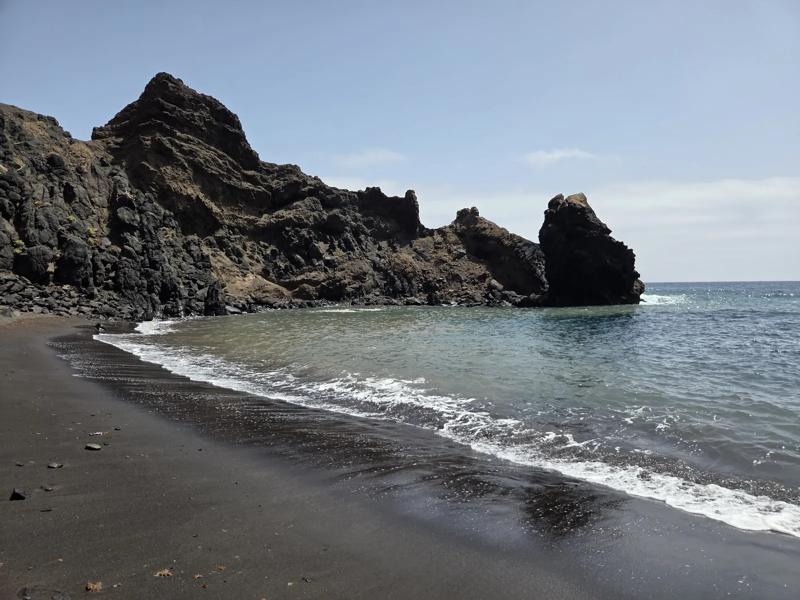 Pequeña playa de arena negra protegida por formaciones rocosas en Roque Bermejo