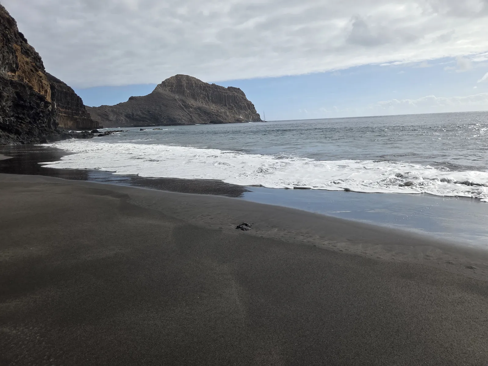 Pequeña cala de arena oscura encajada bajo altos acantilados volcánicos